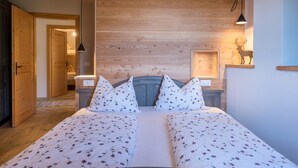 Ein Schlafzimmer mit einem Holzkopfteil, zwei Betten mit floraler Bettwäsche, einem Nachttisch, einem an der Wand montierten Regal mit einer Hirschsilhouette und einer hängenden Leuchte.
