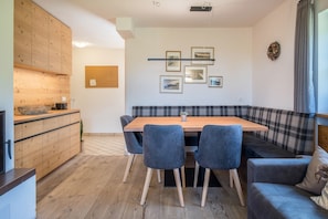 A modern kitchen with wooden cabinets, a dining table with chairs, a bench, and framed pictures on the wall. - Ski-In Vacation Home “Thaleralm” on the Alp with Mountain View, Terrace & Garden (Eggen/Deutschnofen)