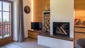 Ein Wohnzimmer mit Kamin, Holzvertäfelung, Fernseher und einem großen Fenster mit Vorhängen.