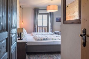 Een slaapkamer met een bed, een nachtkastje, een lamp, een raam met gordijnen en een houten deur.
