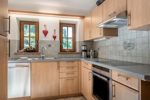 A kitchen with wooden cabinets, a dishwasher, a stove, and a coffee maker. - Ski-In Vacation Home “Thaleralm” on the Alp with Mountain View, Terrace & Garden (Eggen/Deutschnofen)