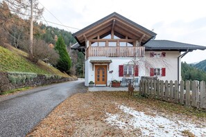 A two-story chalet with a wooden balcony, a stone wall, and a wooden fence.