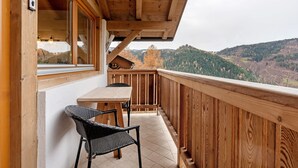 A wooden balcony with a table and chairs, overlooking a mountainous landscape. - Apartment “Thymian - Thalerhof” with Mountain View, Wi-Fi, Balcony & Garden (Eggen/Deutschnofen)