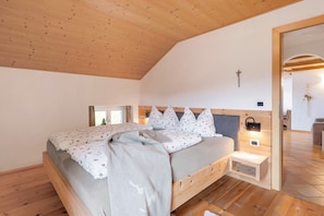 A bedroom with a wooden ceiling, a bed with floral bedding, a bedside table with a lamp, and a small window.