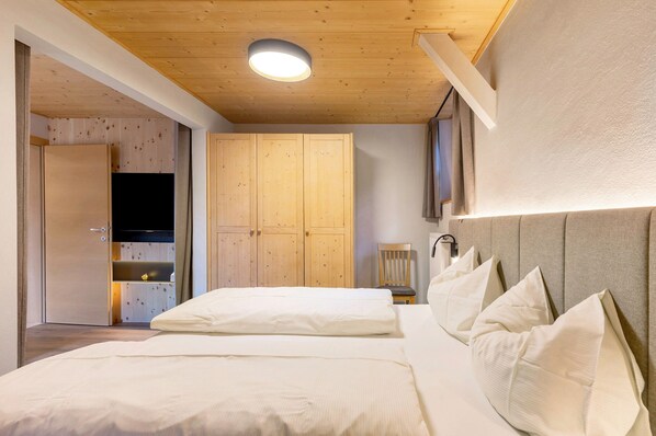 A bedroom with a wooden ceiling, a bed with white bedding, a headboard with multiple pillows, and a wardrobe.