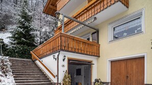 Ein zweistöckiges Gebäude mit einem Holzbalkon, einer Garage und einer verschneiten Landschaft.