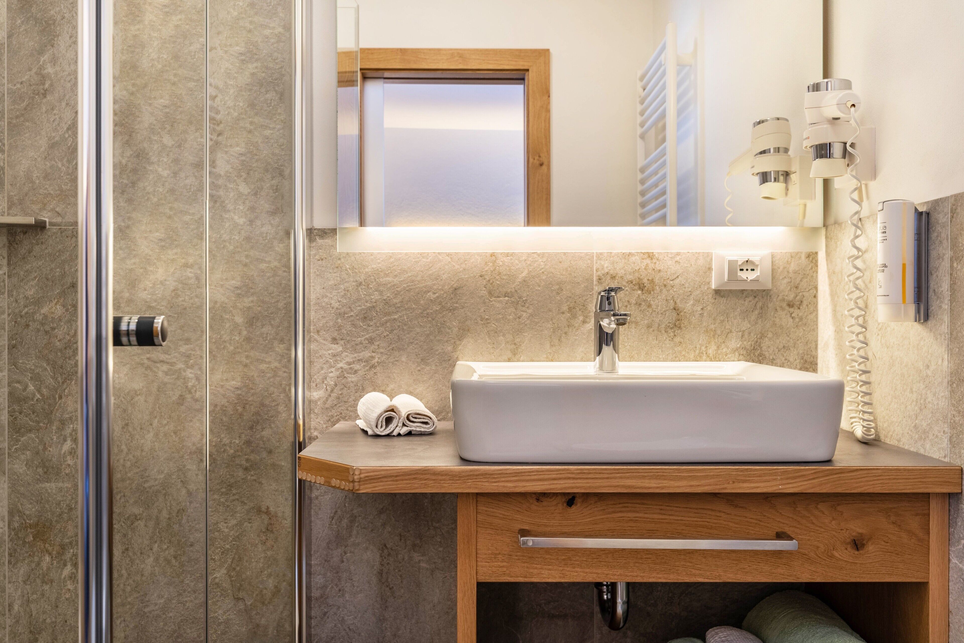 A bathroom with a white sink, wooden vanity, a towel, and a mirror.
