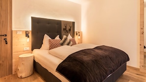 Ein Schlafzimmer mit einem großen Bett, einem hölzernen Kopfteil, zwei Nachttischlampen und einem kleinen Holzschemel.