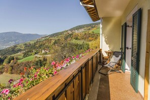 A balcony with a view of a hilly landscape, a chair, and a table.