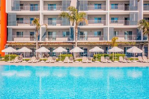 A hotel with a swimming pool, sun loungers, and umbrellas.