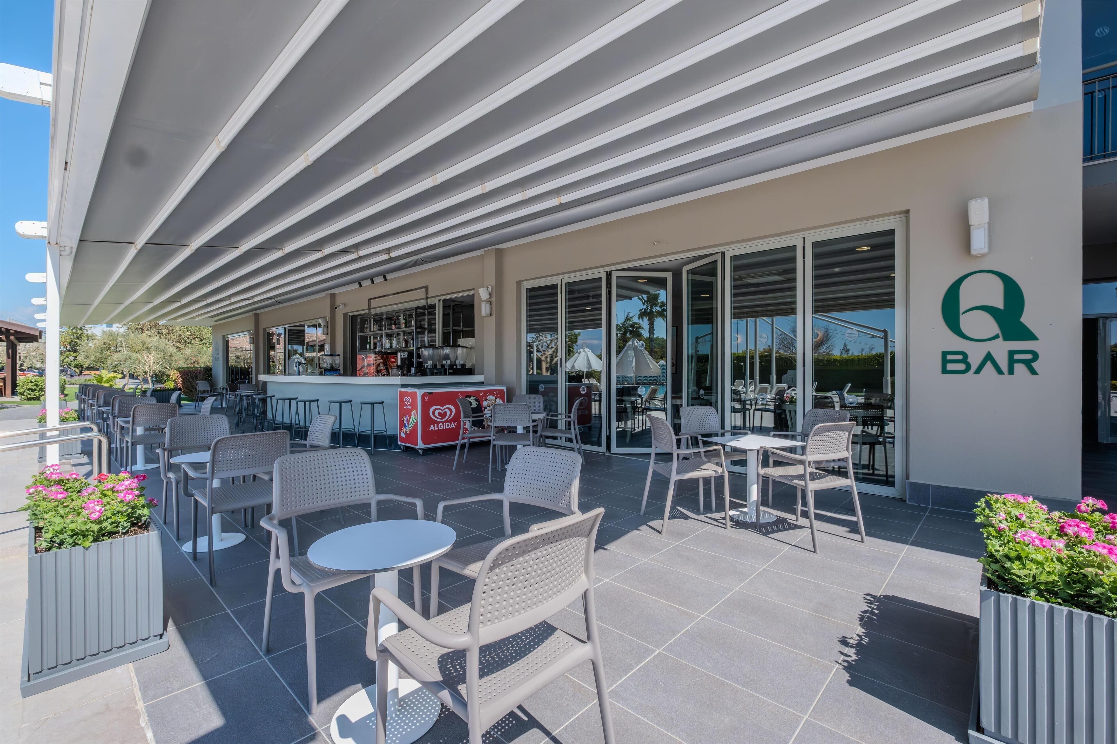 An outdoor patio area with tables and chairs, a bar area with a counter, and a sign that reads "Q BAR".