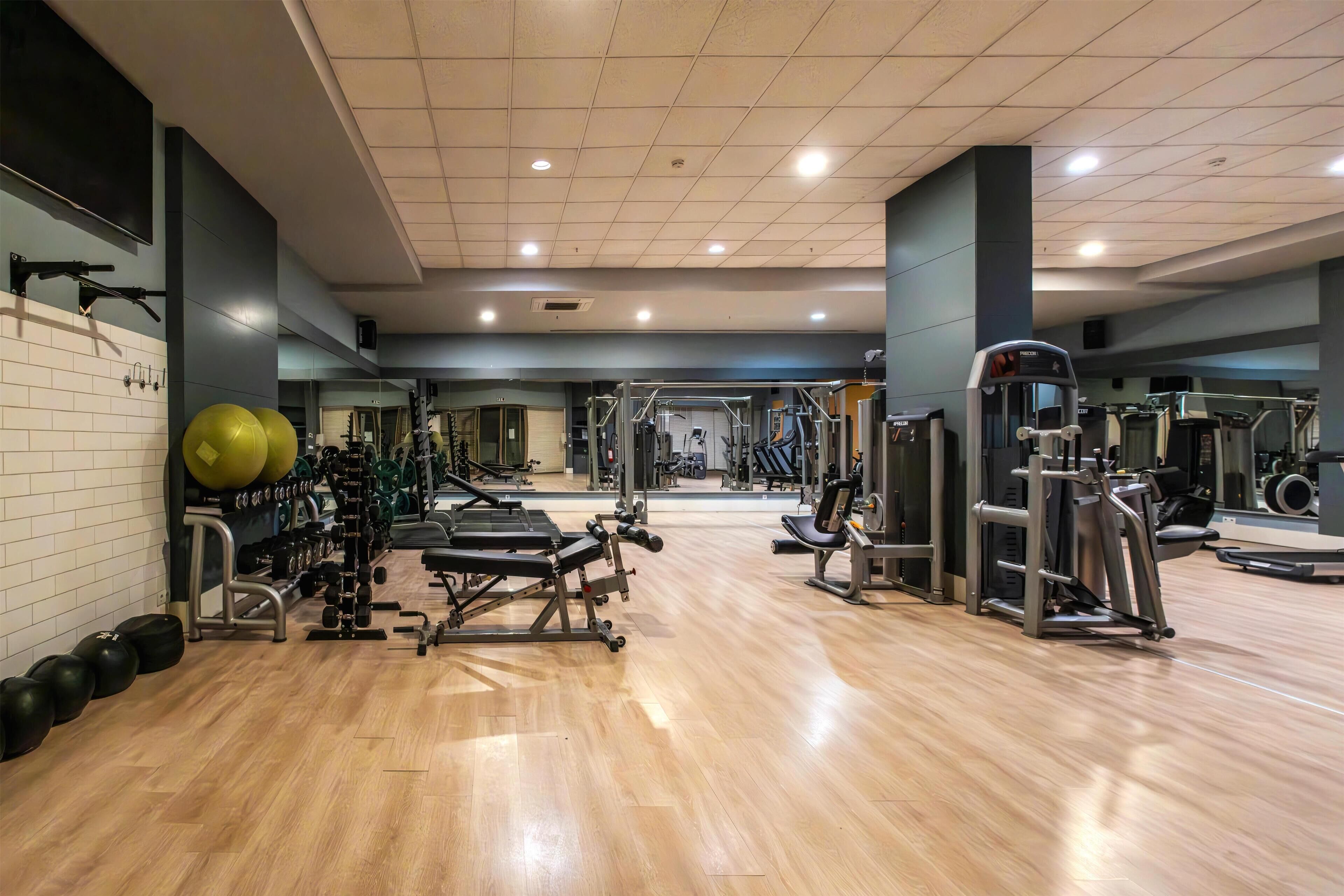 Un gimnasio con equipo de ejercicio, espejos y suelo de madera.