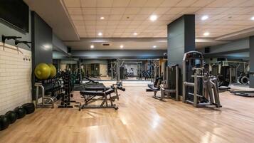 Un gimnasio con equipo de ejercicio, espejos y suelo de madera.