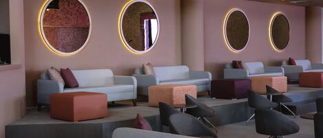 Un espacio lounge moderno con sofás y otomanas dispuestas alrededor de espejos circulares.