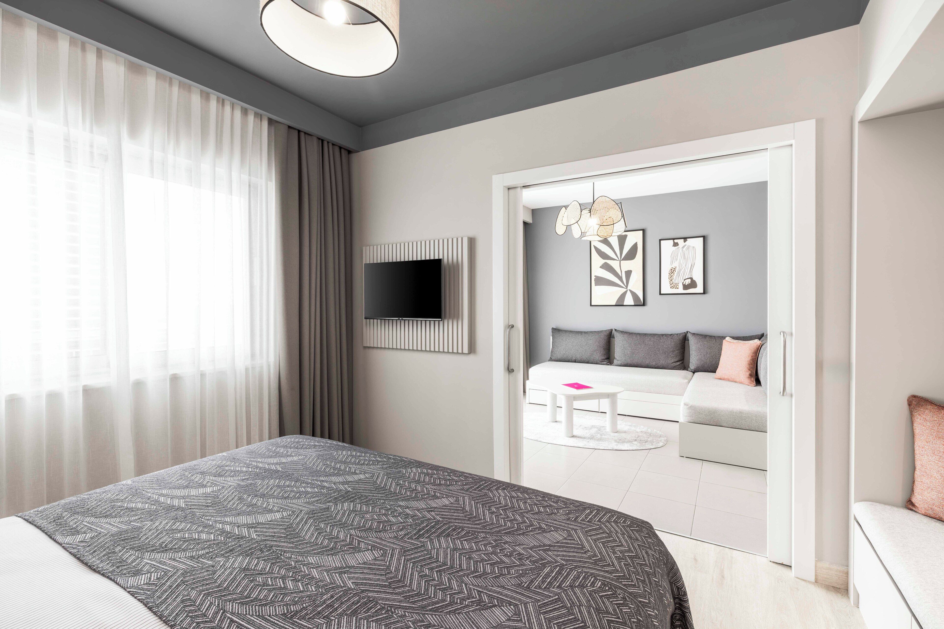 A modern bedroom with a large bed, a TV mounted on the wall, a sofa set, and a dining table.