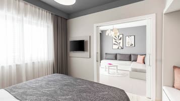 A modern bedroom with a large bed, a TV mounted on the wall, a sofa set, and a dining table.