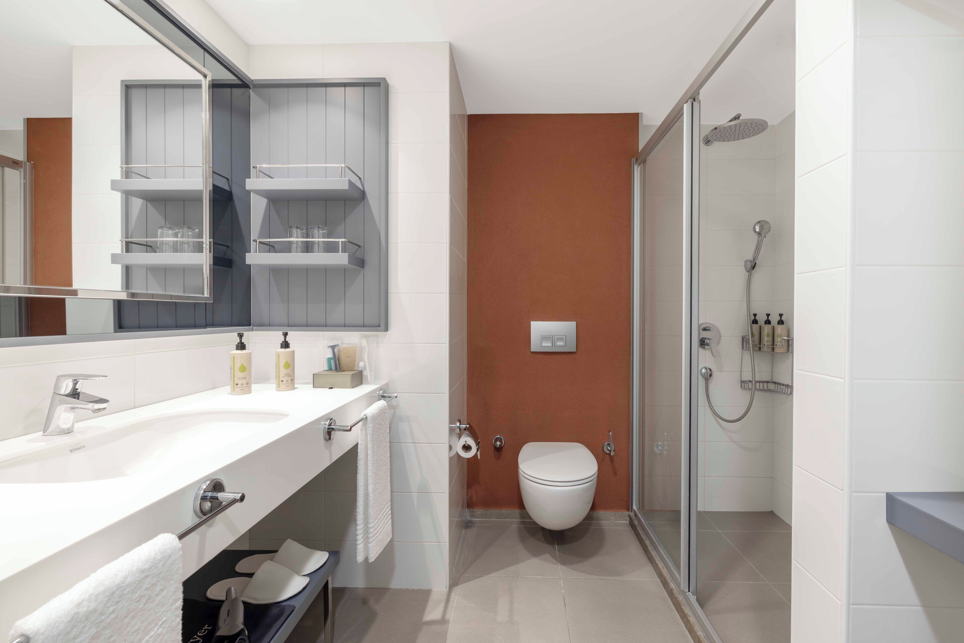 Un baño moderno con lavamanos blanco, espejo y cabina de ducha con mampara de vidrio.