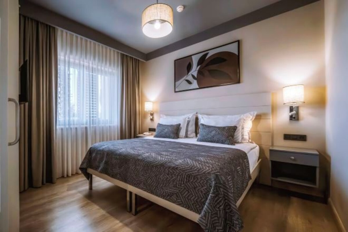 A hotel room with a large bed, bedside lamps, a wall-mounted TV, and a window with curtains.