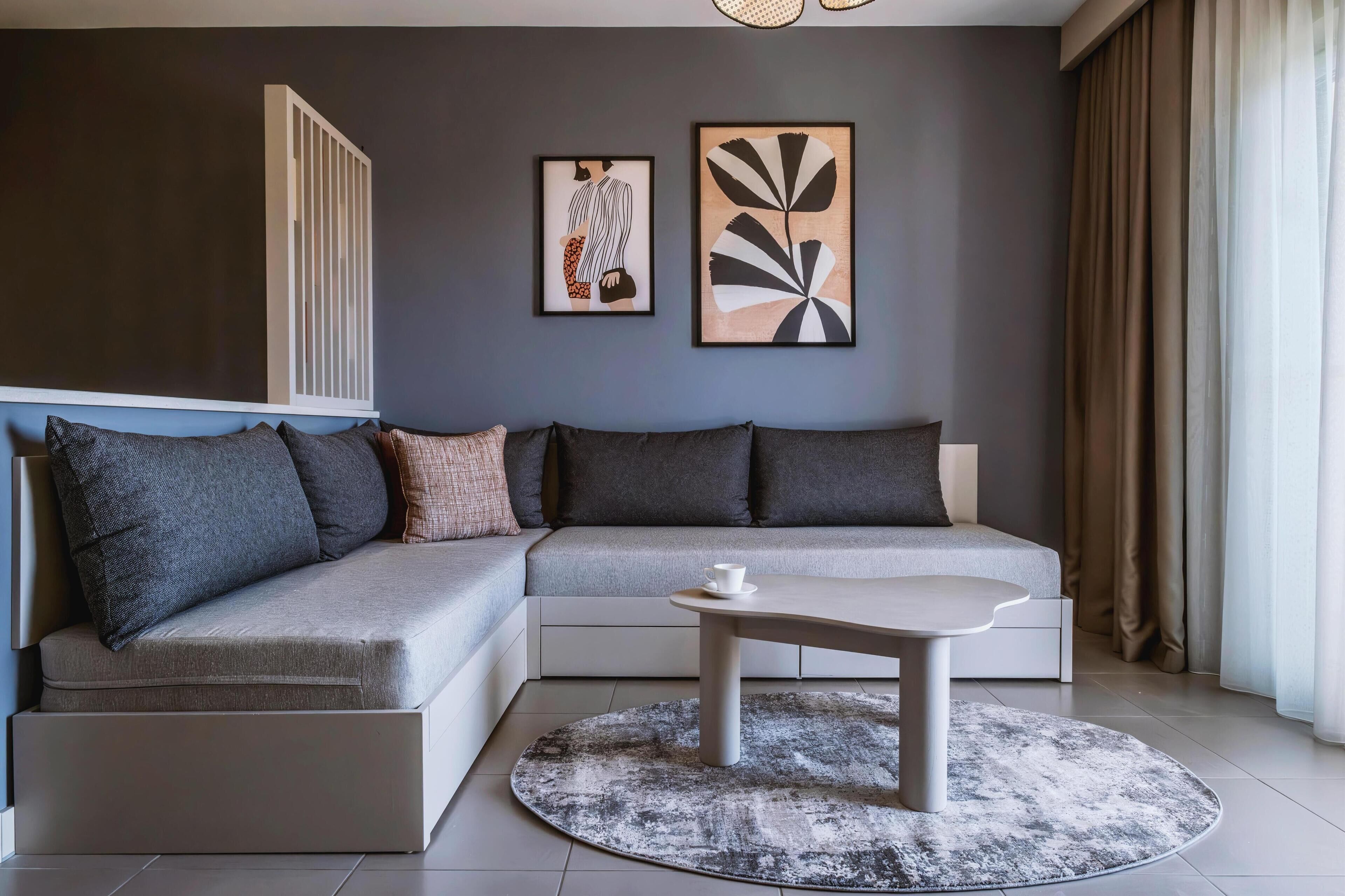A modern living room with a grey sectional sofa, a round coffee table, and two framed artworks on the wall.