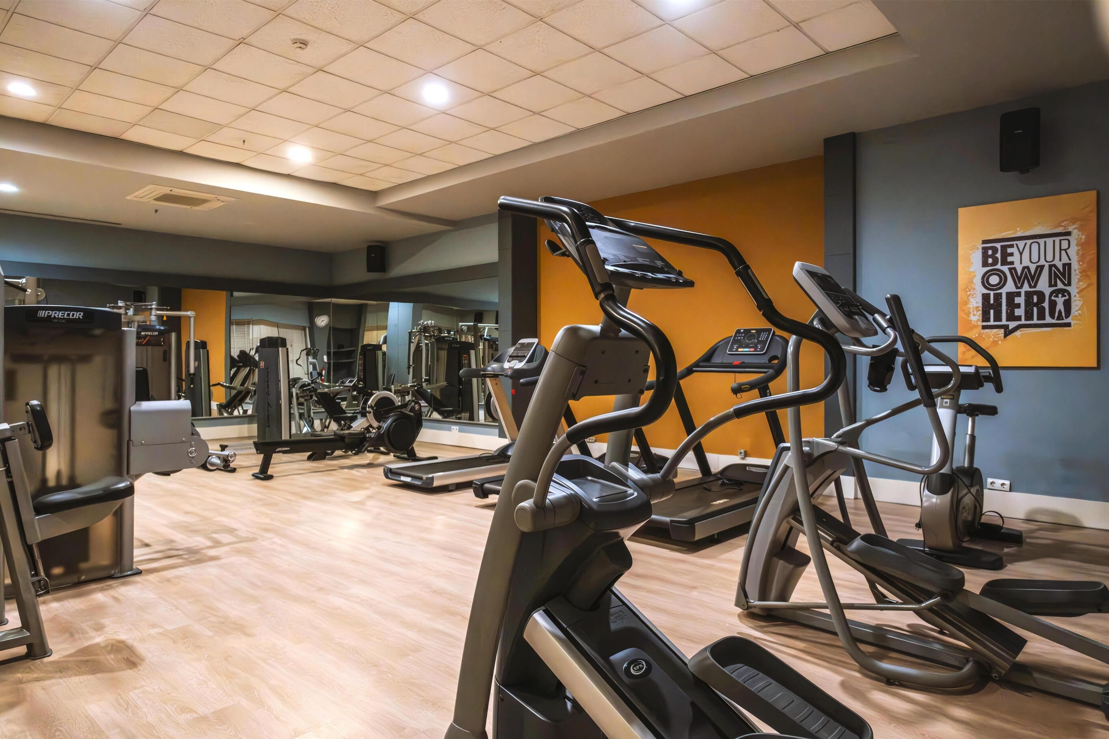 A gym with various exercise equipment, including treadmills and weight machines, and a motivational poster on the wall.