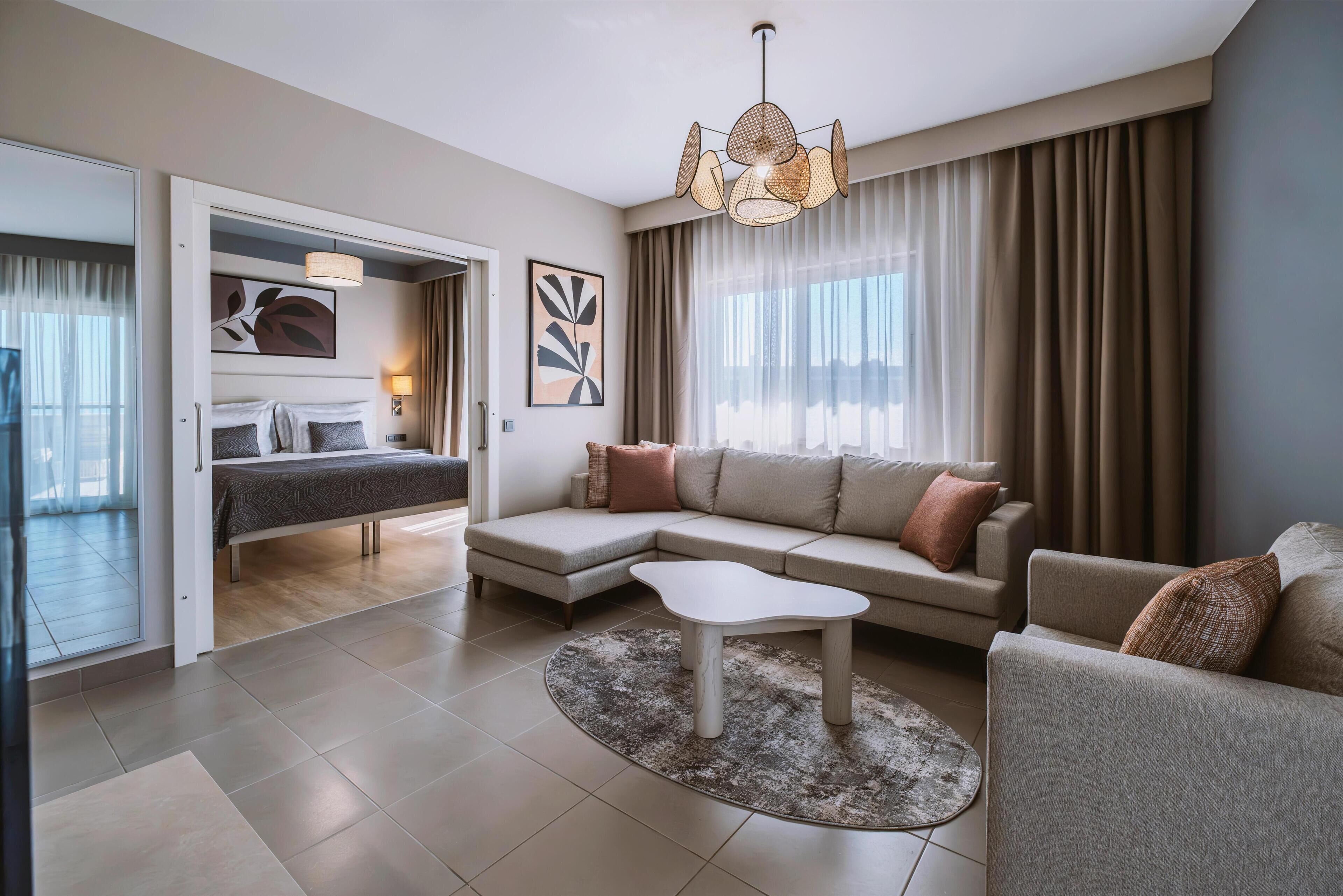 Una habitación de hotel moderna con una cama, un sofá, una mesa de centro y un ventanal con cortinas.