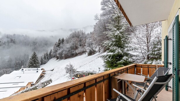 Ein Balkon mit Blick auf eine verschneite Landschaft, einem Tisch und zwei Stühlen.