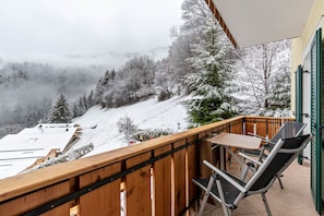 A balcony with a view of a snowy landscape, a table, and two chairs.