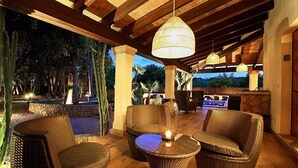 Ein möblierter Patio-Bereich mit Korbmöbeln, einer Hängeleuchte und einer Steinmauer.
