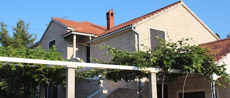 A two-story building with a red-tiled roof and a chimney. There is a covered outdoor area with a pergola and vines.