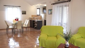 A living room with a green sofa, a dining table with chairs, and a kitchen in the background.