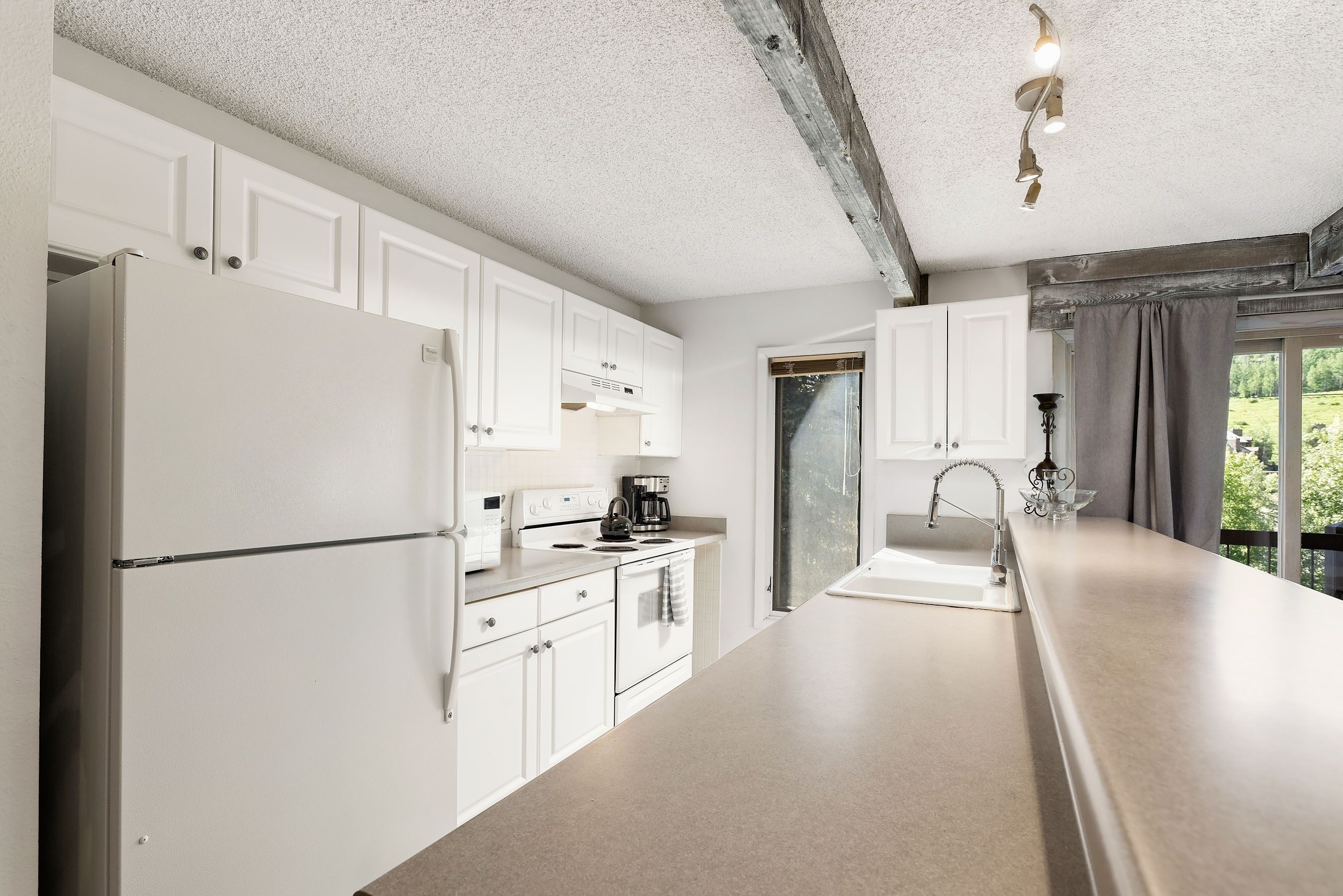 A modern kitchen with white cabinets, a stainless steel refrigerator, and a large countertop.