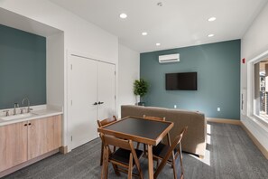 A modern room with a kitchenette, a dining table with chairs, a sofa, and a TV mounted on the wall.