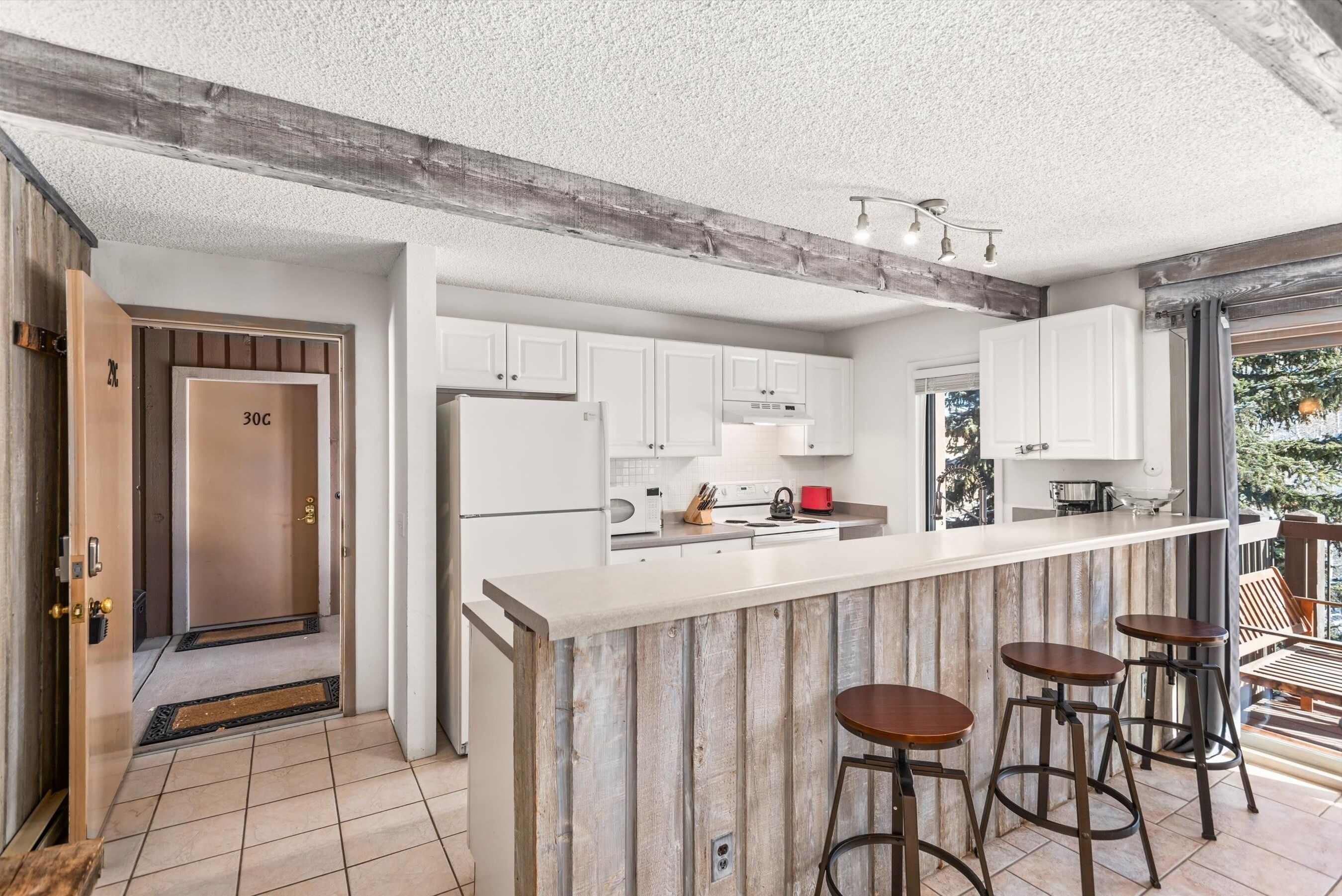 A modern kitchen with white cabinets, a central island with stools, and a wooden ceiling beam.