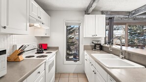 Una cocina moderna con armarios blancos, estufa, pileta y ventana con vista a árboles.