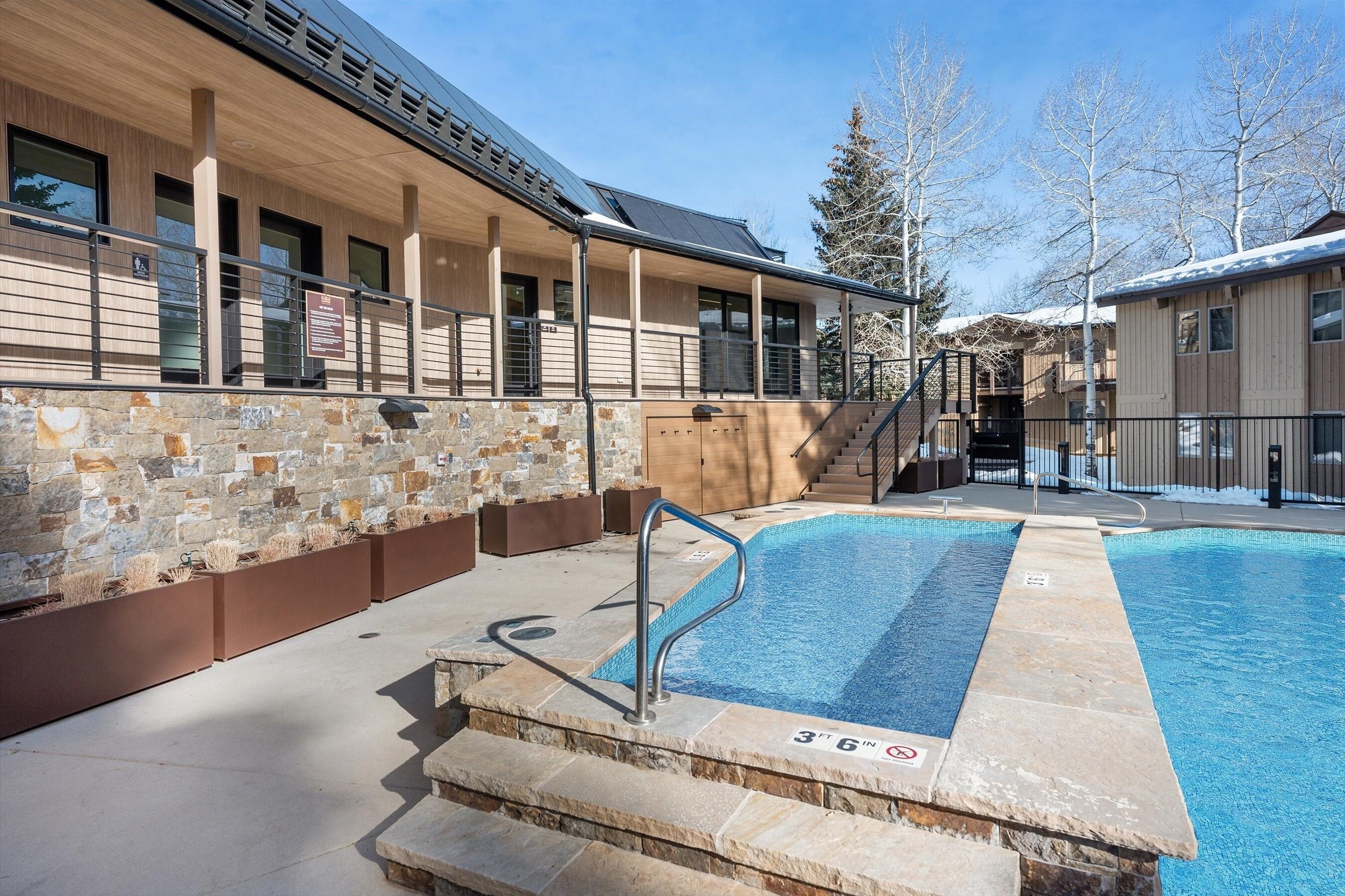 A modern building with a pool area, stone walls, and wooden balconies.