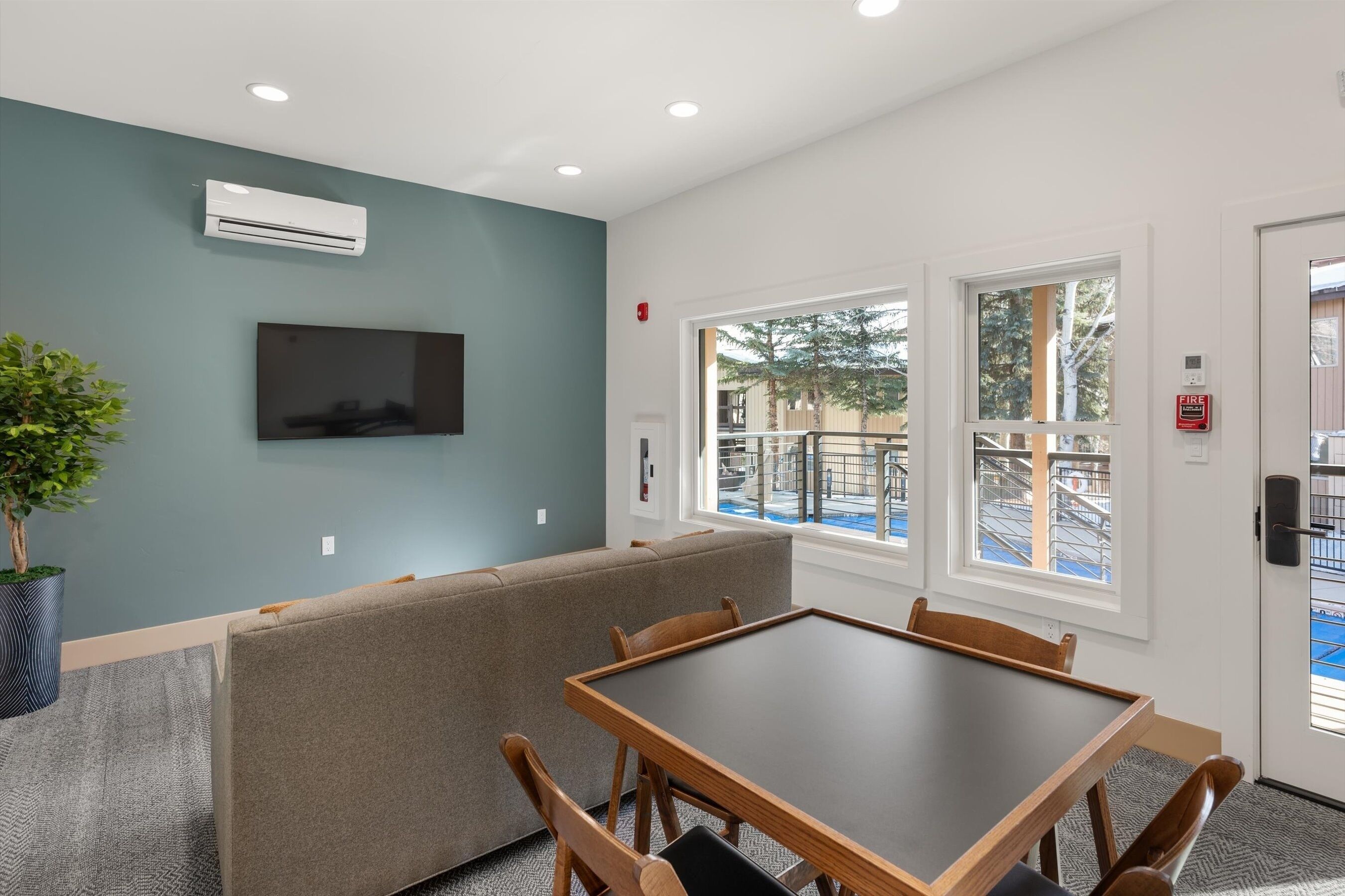 A modern room with a sofa, a table, and a TV. There are windows and a door.