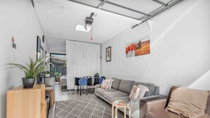 A modern living room with a sofa, a coffee table, a dining area with a table and chairs, and a large window with curtains. - A Private Garage Suite in Forest Lodge (Forest Lodge)