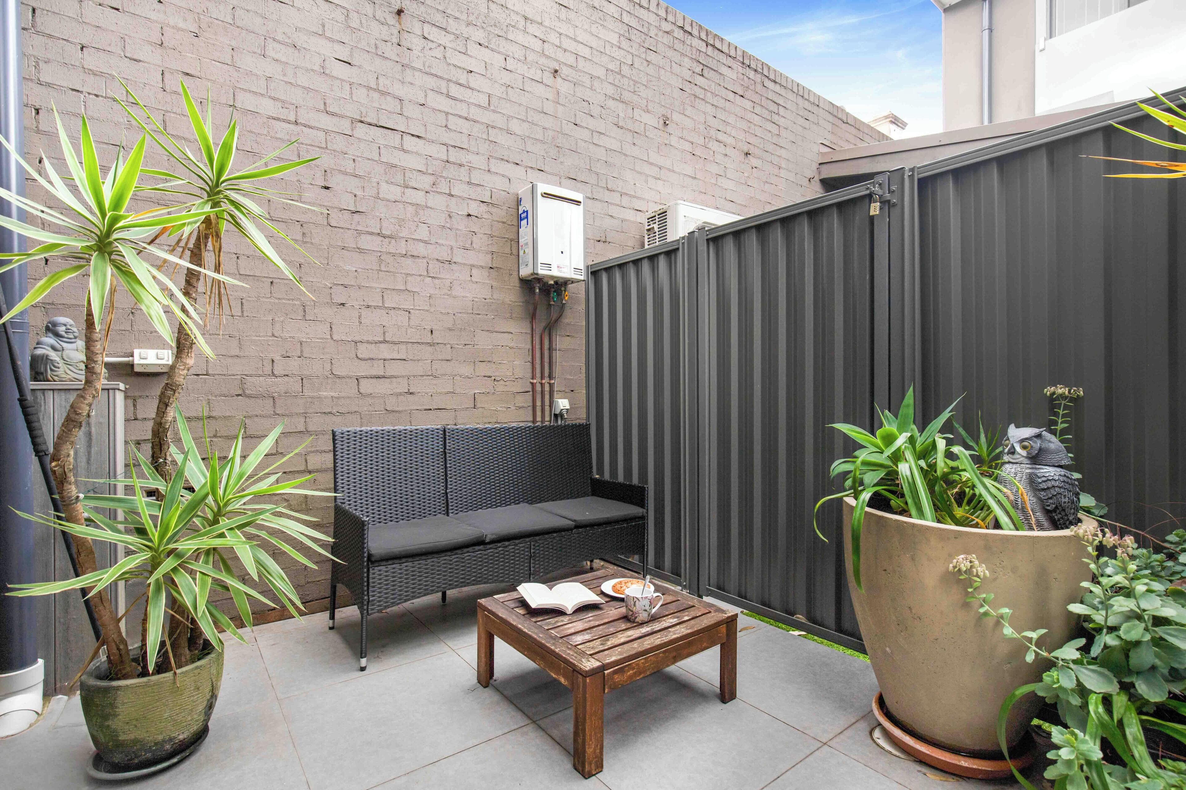 A patio with a wooden table, a black sofa, and a potted plant.