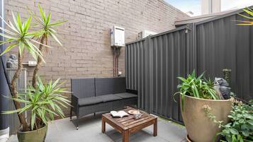 A patio with a wooden table, a black sofa, and a potted plant.