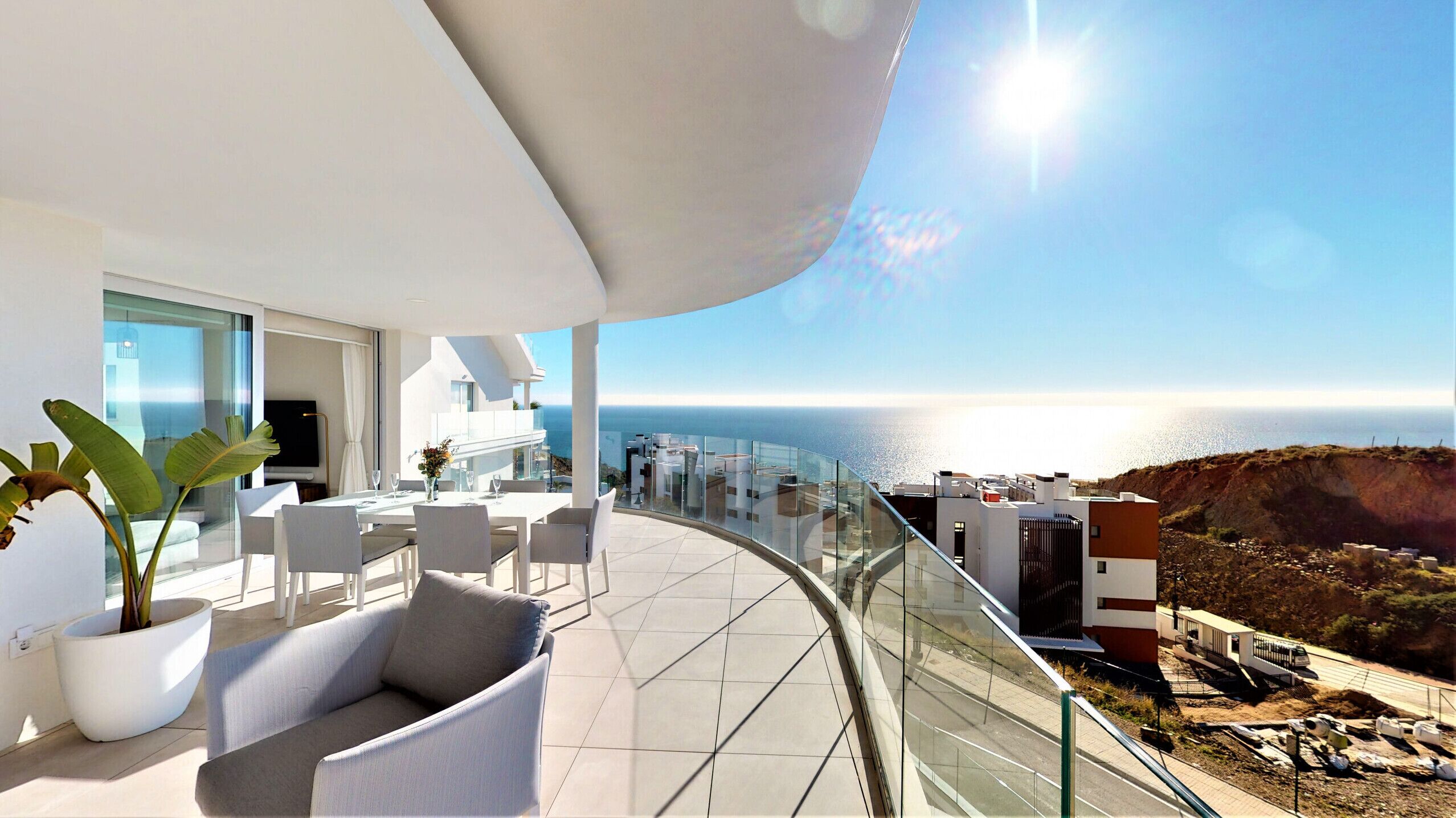Un balcón moderno con barandilla de cristal curvo y vistas al mar.