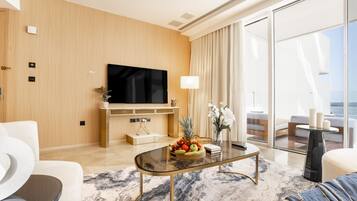 A modern living room with a flat-screen TV, a coffee table with fruit, a sofa, and a view of the outdoors.