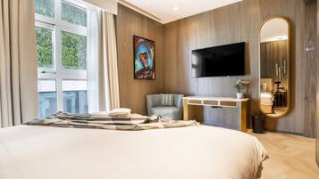 A modern hotel room with a large bed, a flat-screen TV, a seating area, a vanity, and a large mirror.
