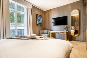 Una habitación de hotel moderna con una cama grande, un televisor de pantalla plana, una zona de estar, un tocador y un espejo amplio.