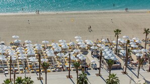 Ein Strandresort mit Reihen von Liegestühlen und Sonnenschirmen, einem Sandstrand und einem klaren, blauen Meer.