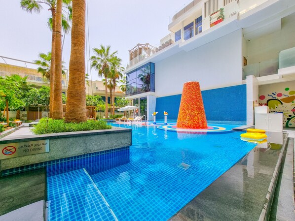 A swimming pool with a no diving sign, surrounded by palm trees and a blue tiled wall.