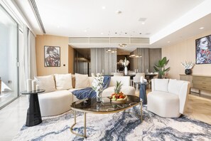 A modern living room with a glass coffee table, beige sofas, and a marble-patterned rug.