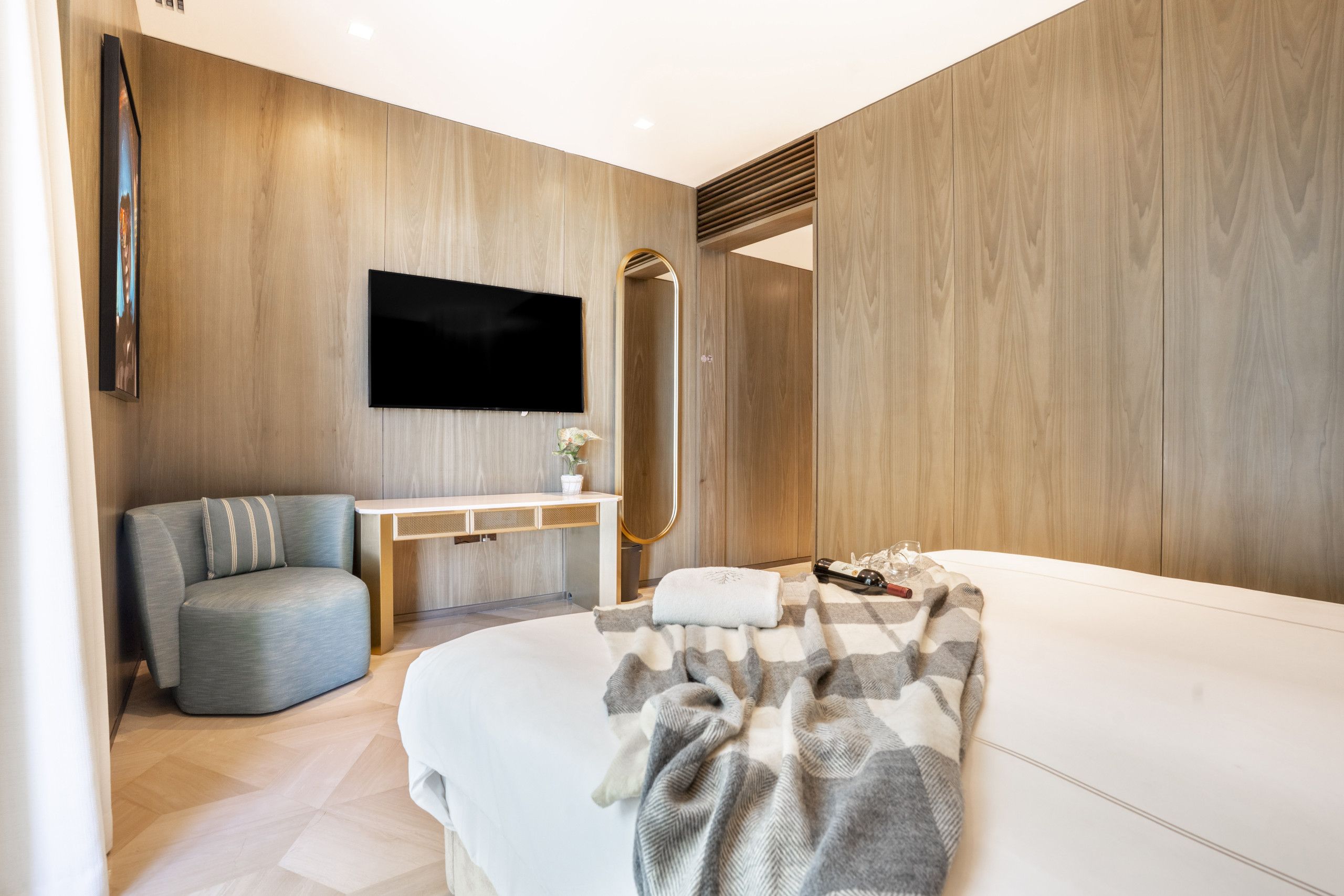 A modern bedroom with a bed, a seating area, a vanity, and a television.