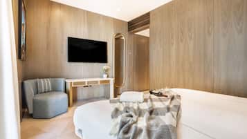 A modern bedroom with a bed, a seating area, a vanity, and a television.