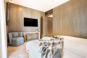 A modern bedroom with a bed, a seating area, a vanity, and a television.