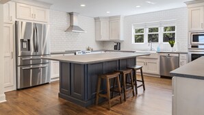 A modern kitchen with white cabinetry, stainless steel appliances, and a central island with stools.
